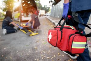 Someone holding a red first aid bag walking towards a person lying on a stretcher.